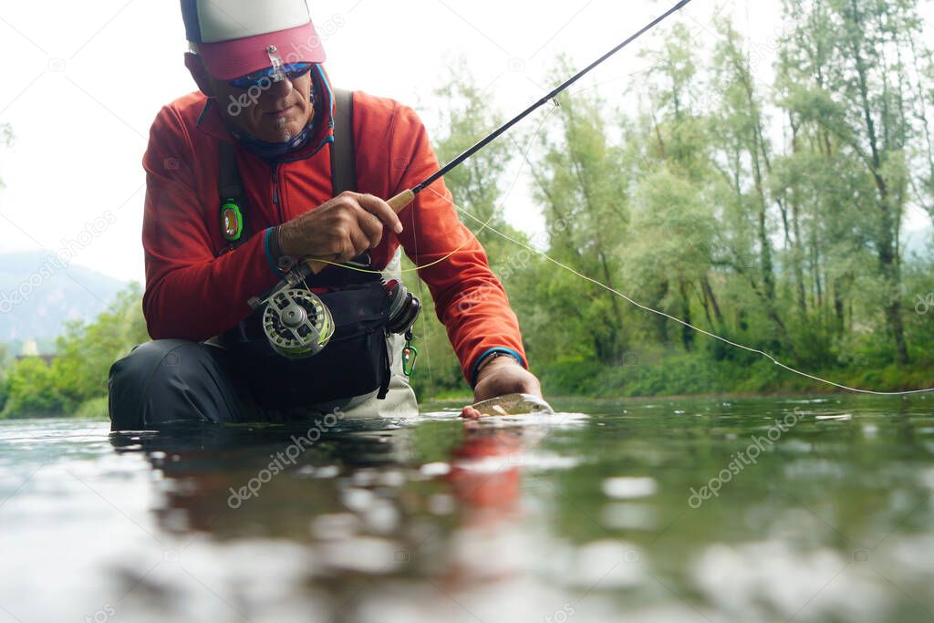 fly fisherman with a red backpack and a red jacket fishing in a high mountain river in summer