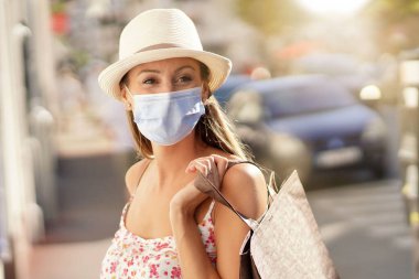 Genç bir kadın turist bölgesinde alışveriş yapıyor, maske takıyor.