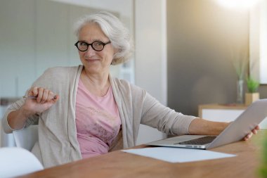 Evde dizüstü bilgisayar kullanan yaşlı bir kadın.