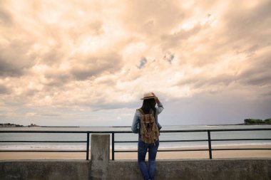 Gün batımında sahilden denize bakan kadının arka görüntüsü.