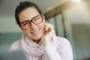 Gülümseyen koyu renk saçlı, gözlüklü kadın dizüstü bilgisayarla çalışıyor.