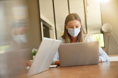 Ofiste çalışan yüz maskeli genç bir kadın.