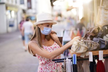 Genç bir kadın turist bölgesinde alışveriş yapıyor, maske takıyor.
