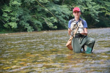 Genç çocuk yazın temiz suyla güzel bir nehirde balık tutuyor.