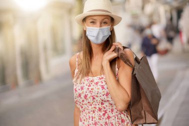 Genç bir kadın turist bölgesinde alışveriş yapıyor, maske takıyor.