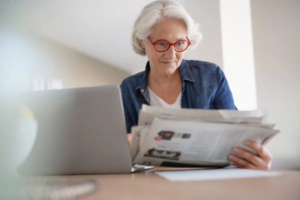 Старша Жінка Читає Газету Перед Ноутбуком — стокове фото