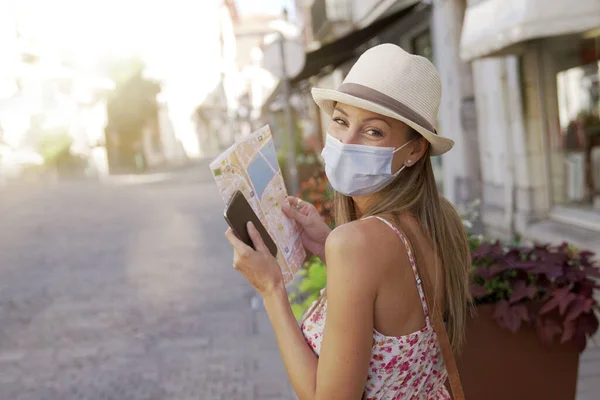 Tourist woman with face mask reading map and using smartphone