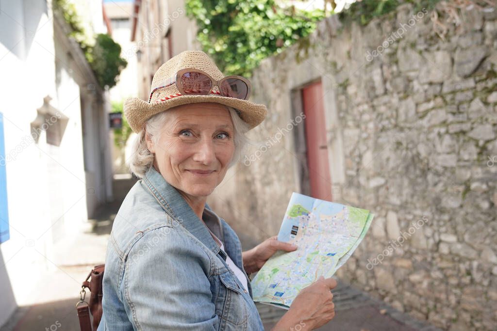 Portrait of senior woman with hat visiting touristic town, reading city map