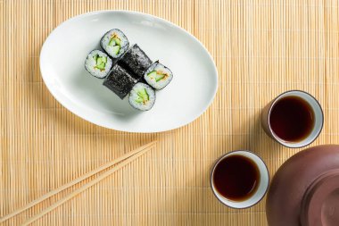 salatalık ve çay iki kap ile küçük suşi roll bir ahşap masa üstü görünümü.