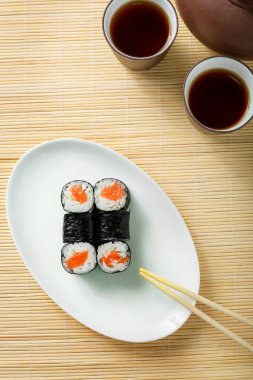 kırmızı balık ve çay iki kap ile küçük suşi roll bir ahşap masa üstü görünümü.