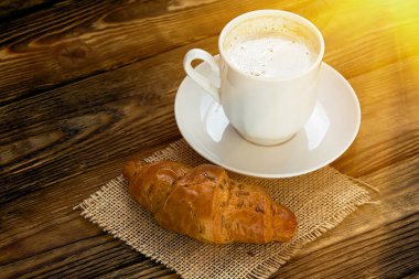 beyaz ile krem şanti ve çörek güneş ışığı altında koyu ahşap bir masa üzerinde sıcak kahve fincan