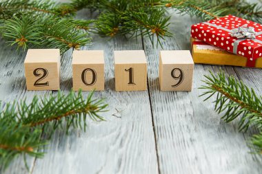 çam dalları ve hediyeler yanında gri bir ahşap zemin üzerinde yılın rakamları ile tahta küpleri