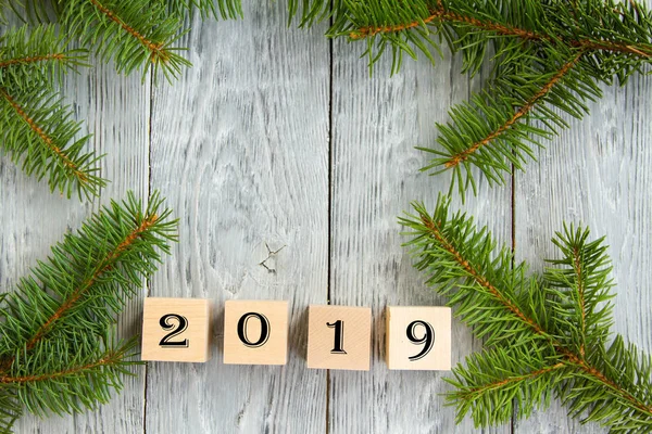 New year\'s holiday card. wooden cubes with figures of the year on a gray wooden background, next to fir branches.Concept of winter holiday