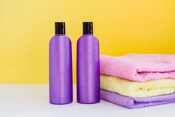 two purple cosmetic bottles and three bath towels for Spa treatments and body and hair care