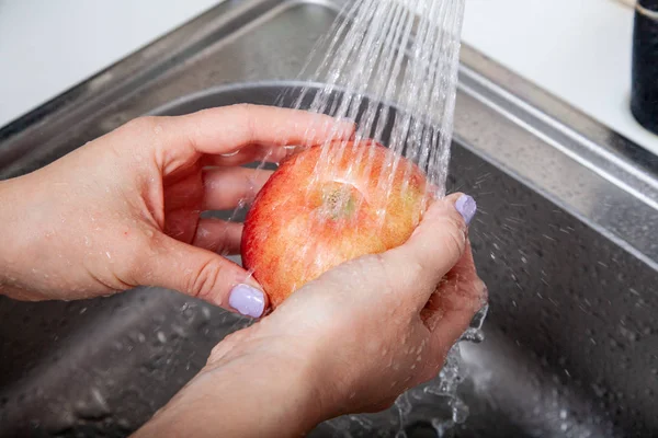 female hand wash up a red ripe Apple