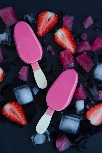 Two pink ice cream on a black background next to the sliced strawberries and chopped ice. Summer cold desert — Stock Photo, Image