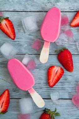 dilimlenmiş çilek ve doğranmış buz yanında ahşap bir arka plan üzerinde iki pembe dondurma