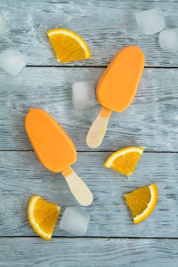 dilimlenmiş portakal meyve ve doğranmış buz yanında ahşap bir arka plan üzerinde iki sarı dondurma