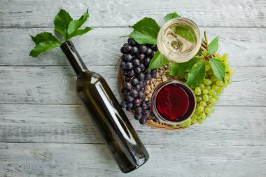 Koyu ve yeşil üzüm kümesi ve kırmızı ve beyaz şaraplı iki şarap kadehi, yuvarlak bir tepside şişe ve gri ahşap masa. Şarap kompozisyonu düzdü..