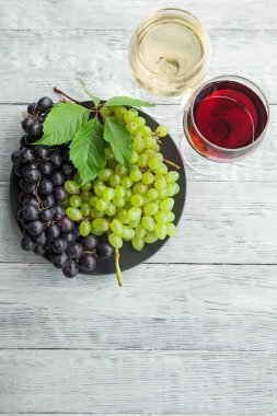Siyah yuvarlak bir tabak üzerinde koyu yeşil üzüm ve iki şarap kadehi ve gri ahşap masa, üst manzara ve kopyalama alanı..