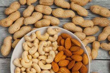 Bir avuç soyulmuş badem ve beyaz tabakta kaju fıstığı. Yakın çekim ve üst görünüm