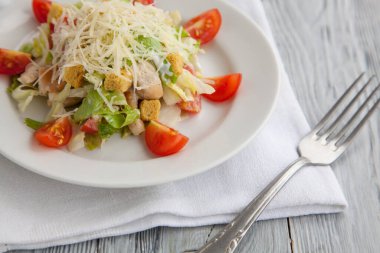 Tahta arka planda beyaz tabakta Sezar salatası. Menü tabakları. Domates dilimleriyle süslenmiş salata ve üzerine peynir serpiştirilmiş.