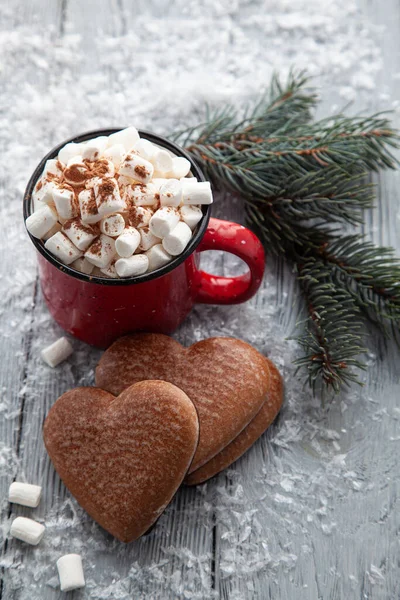 Xícara de cacau quente com marshmallows e pão de gengibre de Natal na forma de um coração em um fundo de madeira nevado. — Fotografia de Stock