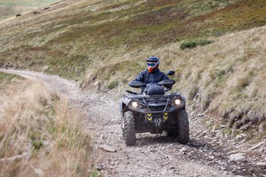 Front view of quad bike zipping along a country road in Carpathian mountains, Ukraine. clipart