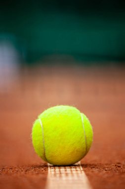 Sarı bir tenis topu toprak kortta yatıyor..