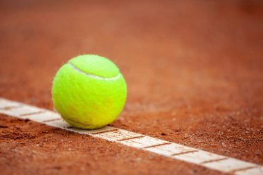 Sarı bir tenis topu toprak kortta yatıyor..