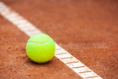 Sarı bir tenis topu toprak kortta yatıyor..
