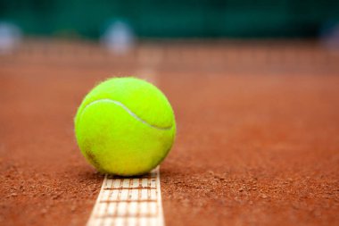 Sarı bir tenis topu toprak kortta yatıyor..