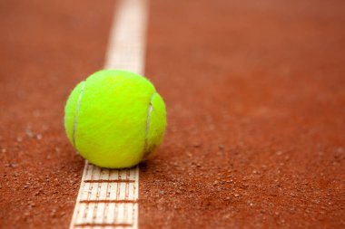 Sarı bir tenis topu toprak kortta yatıyor..