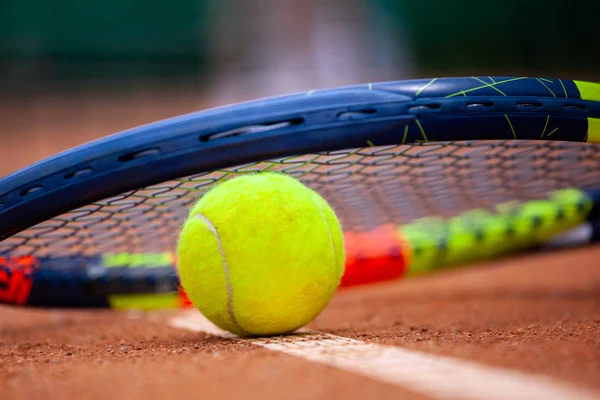 Yellow tennis ball and racket lie on the clay court. — Stock Photo, Image