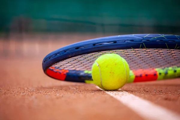 Yellow tennis ball and racket lie on the clay court.