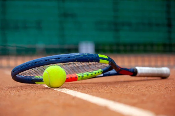 Yellow tennis ball and racket lie on the clay court. — Stock Photo, Image