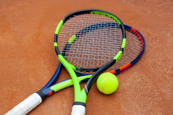 Two tennis rackets and yellow tennis ball lie on the clay court. — Stock Photo, Image