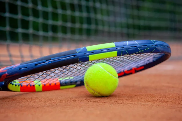 Yellow tennis ball and racket lie on the clay court. — Stock Photo, Image