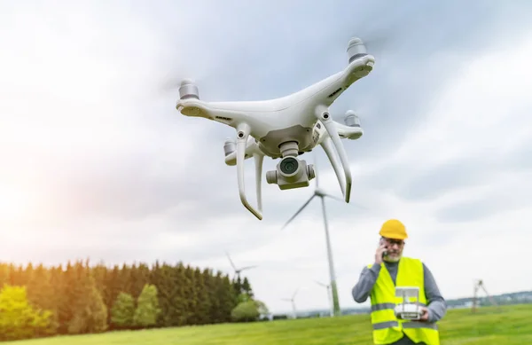 Drone operated by construction worker inspecting wind turbine, flying with drone.
