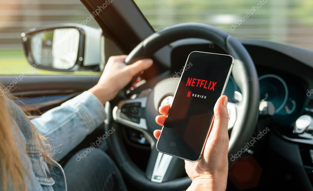AACHEN, GERMANY - 31. August 2019 : Netflix app on Apple iPhone in car. Young man is browsing the movie video library what to watch.