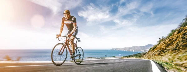 Volwassen volwassene op een racefiets klimmend over de heuvel aan de Middellandse Zee — Stockfoto