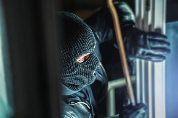 Masked burglar with torch and crowbar breaking and entering into — Stock Photo, Image