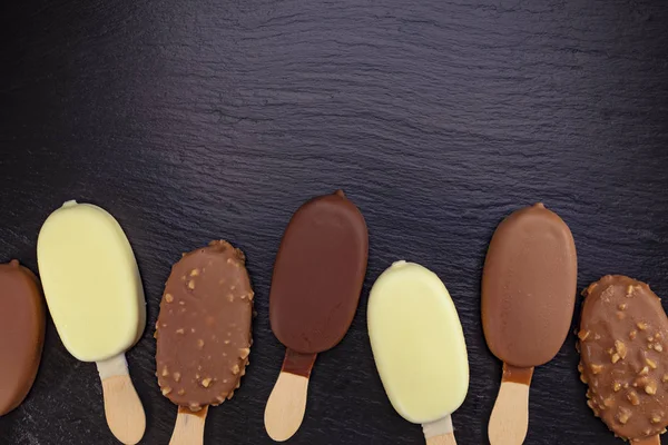 ブラックストーンスレートボード上のチョコレートで覆われたスティック上のアイスクリーム — ストック写真