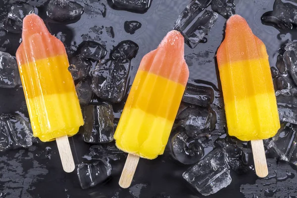 スティック ブラック スレート ボード上の氷の上にフルーツ アイス クリーム アイスキャンディーに焦点を当てる — ストック写真