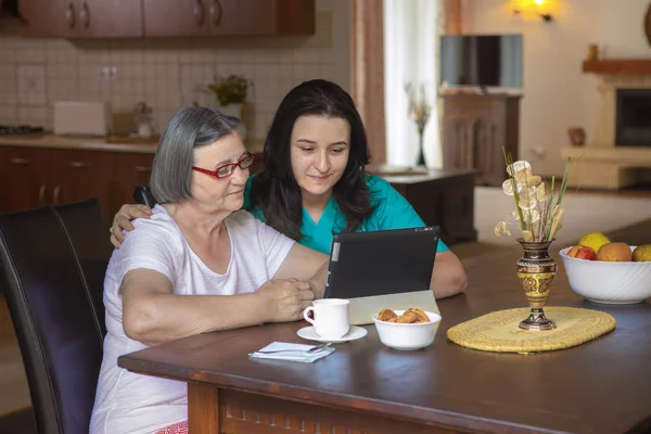 Θηλυκό Νοσοκόμα Και Ανώτερων Γυναίκα Που Χρησιμοποιούν Tablet Στην Κουζίνα — Φωτογραφία Αρχείου