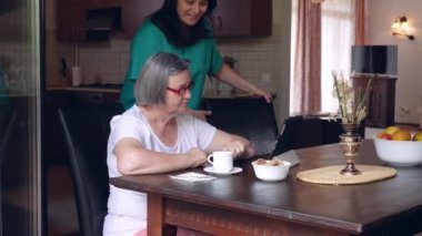 Kadın hemşire ve üst düzey kadın kullanarak tablet Pc bakım evi, mutfakta. El hareketi 4k