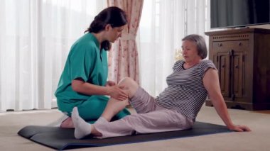 Veren bacak masaj için bir emeklilik ev kadın kıdemli hemşire. Bir yaşlı kadın fiziksel rehabilitasyon evde yardım fizyoterapist hemşire. Yavaş hareket 4k el hareketi