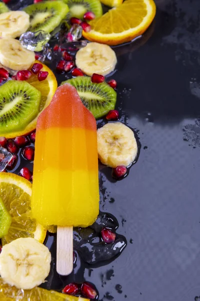 Fruit ice cream on stick with slices fruits on black slate — Stock Photo, Image