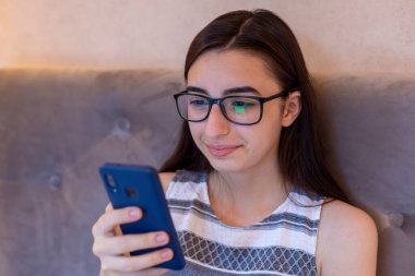 Gözlüklü genç beyaz kız koltukta oturup internette geziniyor, gözlüklü bir kadın akıllı telefondan mesaj yazıyor, haberleri okuyor ya da internetten alışveriş yapıyor.