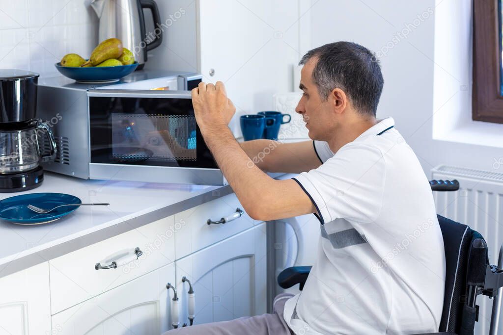 Young Man in Whellchair Using Microwave Oven For Baking In Kitchen. Focus on his hand.